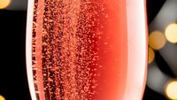 Sparkling pink champagne or rosé wine in elegant glass with bubbles against blurred bokeh lights background for celebration and festive occasions.
