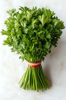 Fresh parsley bunch tied with red ribbon on white marble background, vibrant green herb for cooking and garnishing. Close up view shows crisp leaves and stems.
