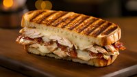 Grilled panini sandwich with turkey, bacon and melted cheese on wooden cutting board. Delicious hot pressed sandwich for restaurant menu and food photography.