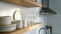 Modern kitchen interior with wooden shelves displaying white dinnerware, wine glasses and ceramic dishes against subway tile backsplash for home design.