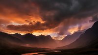 Dramatic mountain valley landscape with intense orange and purple sunset sky, golden light rays breaking through storm clouds, moody atmospheric scenery for nature and travel projects.