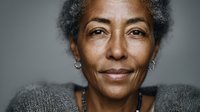 Close-up portrait of senior African American woman with gray hair wearing knitted sweater against neutral background, conveying wisdom and confidence.