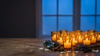 Glowing candles in glass holders create warm ambiance on wooden table with Christmas ornaments and pine branches near window at twilight for holiday decor.