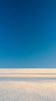 Serene coastal landscape with pristine sandy beach, calm shallow waters, and clear blue sky gradient. Minimalist seascape composition for travel and wellness design projects.