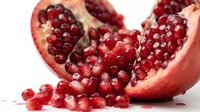 Fresh ripe pomegranate cut in half with ruby red arils spilling out on white background. Healthy organic fruit rich in antioxidants for nutrition and wellness concepts.