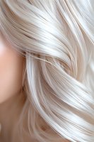 Close-up of platinum blonde wavy hair showing silky smooth texture and natural shine against neutral background, highlighting professional hair care and styling results.