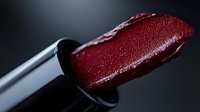 Deep burgundy lipstick bullet with creamy texture shown in macro detail against dark background, showcasing rich pigmentation and glossy finish for beauty and cosmetic marketing.