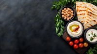 Middle Eastern appetizer spread with creamy hummus, grilled pita bread, chickpeas, fresh herbs and cherry tomatoes on dark background, copy space for menu.