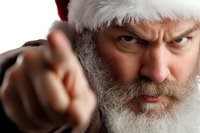 Angry Santa Claus pointing finger at camera with stern disapproving expression, white beard and red hat, close-up portrait on dark background.