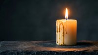Burning candle with melted wax dripping down sides creates warm atmospheric lighting on dark wooden surface for relaxation and meditation concepts.