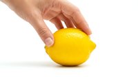 Hand holding a fresh yellow lemon isolated on white background, showcasing vibrant citrus fruit for food, health, and cooking concepts.