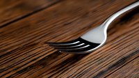 Shiny silver fork on dark wooden table surface with dramatic lighting and shallow depth of field creates minimalist dining composition.