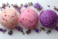 Three scoops of colorful ice cream in pink and purple shades decorated with fresh violet flowers on white background, arranged in minimalist style.