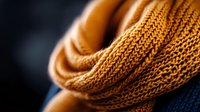 Cozy knitted mustard yellow scarf with detailed wool texture in macro shot against dark background, showing intricate stitch pattern and warm winter fabric details.