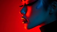 Young Asian woman with gold metallic lipstick in dramatic red and blue lighting, profile view showing sensual expression. Creative beauty portrait for cosmetic advertising.