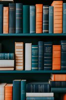 Vintage hardcover books arranged on wooden shelves in teal blue, orange, and white colors creating aesthetic library composition with classic binding spines.