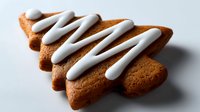 Festive tree-shaped gingerbread cookie with white icing zigzag decoration on neutral background, perfect for holiday season baking and dessert concepts.