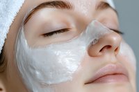 Young Caucasian woman with white facial mask during spa treatment, eyes closed and wearing towel, close up view showing skincare and beauty routine.