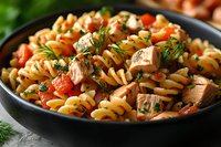 Fusilli pasta with grilled chicken chunks, cherry tomatoes and fresh dill in black bowl. Homemade Mediterranean style dinner with herbs and olive oil.