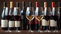 Elegant wine glasses filled with red and white wine arranged in row against collection of wine bottles, creating sophisticated wine tasting presentation.