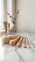 Professional makeup brushes with rose gold handles arranged on marble surface in minimalist bathroom setting with natural lighting and eucalyptus decor.
