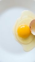 Fresh cracked egg with bright yellow yolk and clear white on clean surface for cooking and baking recipes.