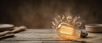 Vintage Edison bulb glowing with warm light and creative energy sparks on rustic wooden surface for innovation and inspiration concepts.