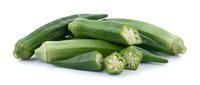 Fresh green okra pods with sliced pieces showing star-shaped cross sections isolated on white background for healthy cooking and nutrition concepts.