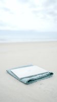 Blank notebook with light blue linen cloth on sandy beach with overcast sky, suitable for travel writing, journaling, creativity, and coastal lifestyle concepts.