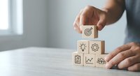 Business professional stacking wooden blocks with strategy icons including target, lightbulb, gear, growth chart and team symbols for goal achievement.