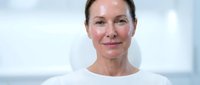 Middle-aged Caucasian woman with natural skin showing confidence and maturity in white top against soft blue background for wellness and aging concepts.