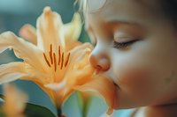 Young Caucasian girl with closed eyes gently smelling peach-colored lily flower in soft dreamy lighting against turquoise background, capturing innocent childhood moment.