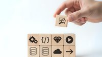 Hand placing wooden cube with magnifying glass icon above row of technology symbols representing search optimization and digital solutions.