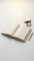 Open notebook with blank pages and a brass pen beside it, accompanied by a small bull figurine on white background, suitable for business, finance, and planning concepts.