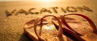 Flip flops on golden sandy beach with vacation text written in sand, warm sunset light, summer holiday travel concept.