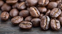 Fresh roasted coffee beans scattered on rustic wooden surface, showing rich brown color and distinctive crack lines, macro close-up with selective focus.