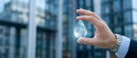 Businessman hand holding water drop against modern office building background representing environmental sustainability and corporate responsibility.