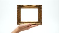 Ornate golden baroque frame held in open palm against white background, isolated for design projects and artistic presentations.