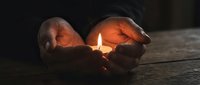 Cupped hands protecting glowing candle flame in darkness creating warm spiritual atmosphere for meditation and hope concepts.