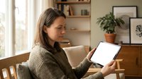 Woman with long dark hair and medium skin tone working on laptop in bright home office with plants and shelves, suitable for business, technology, and remote work concepts.