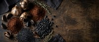 Dark chocolate pieces with cocoa powder, coffee beans and spices arranged in rustic wicker basket on wooden background for gourmet cooking and baking.