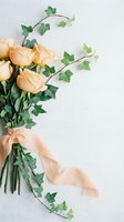 Elegant peach roses bouquet with ivy vines and silk ribbon on white marble background for wedding invitations and romantic greeting cards.