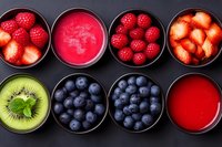 Fresh berries, kiwi slices, and fruit smoothies arranged in black bowls on dark background. Healthy breakfast ingredients and antioxidant-rich foods for clean eating.