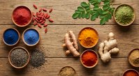 Colorful spices and herbs arranged in wooden bowls on rustic table with fresh ginger, moringa leaves and goji berries for cooking and natural medicine.