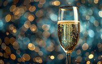 Glass of sparkling champagne with golden bubbles against blurred bokeh lights background in blue and gold tones, festive celebration atmosphere.