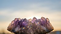 Amethyst crystal cluster glowing against a soft sunset sky, with light refracting through purple quartz points in a stunning natural display.