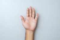 Caucasian male hand raised showing palm against light gray background, minimalist composition demonstrating greeting, voting, or stop gesture.