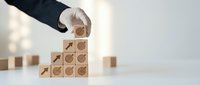 Businessman hand placing wooden blocks with target and arrow symbols creating growth steps concept for business strategy and goal achievement.
