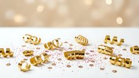 Golden metallic 2025 numbers scattered on white surface with confetti and warm bokeh lights background for New Year celebration and party decoration.