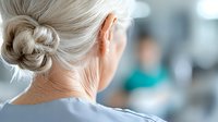 Rear view of senior woman with gray hair in bun at medical facility, showing neck and shoulders in soft focus background, healthcare concept.